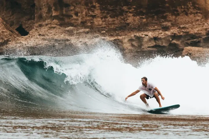 Surfing Destination with a man on a wave in the background rock formation | Picture by Oliver Sjöström